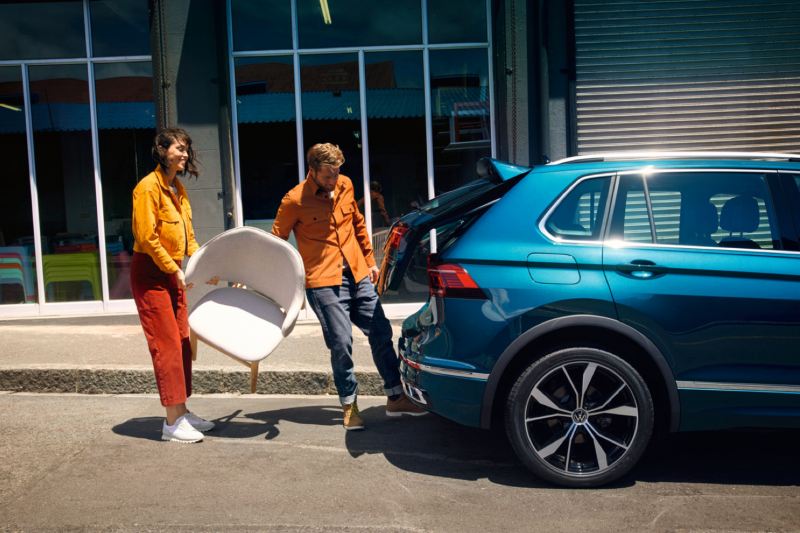 Una pareja con unas silla abriendo el portón trasero de un Volkswagen Tiguan eHybrid azul