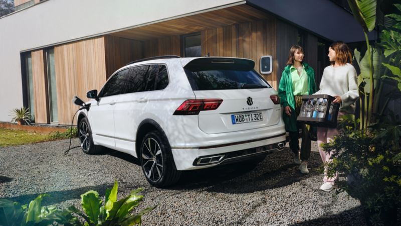Dos chicas caminando detrás de un Volkswagen Tiguan híbrido enchufable aparcado y conectado a un Wallbox