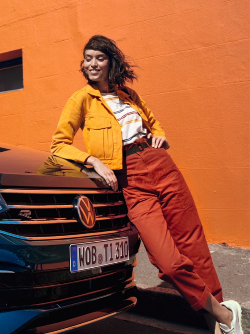 Chica apoyada en el capó de un Volkswagen Tiguan eHybrid con un muro naranja de fondo