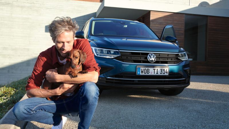 Hombre abrazando su perro, delante de un Volkswagen Tiguan