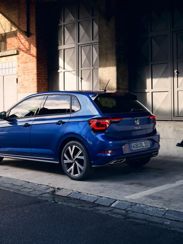 Una chica junto a un Volkswagen Polo de color azul estacionado en la calle