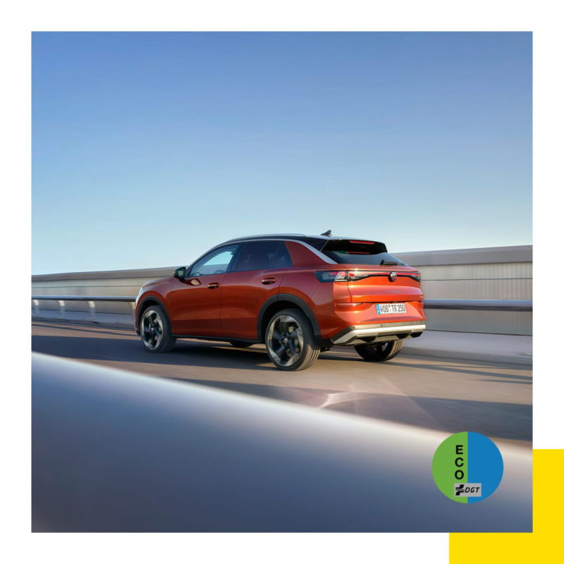 Un Nuevo T-Roc rojo visto de tres cuartos desde atrás en una autopista junto al mar y la etiqueta ECO de la DGT