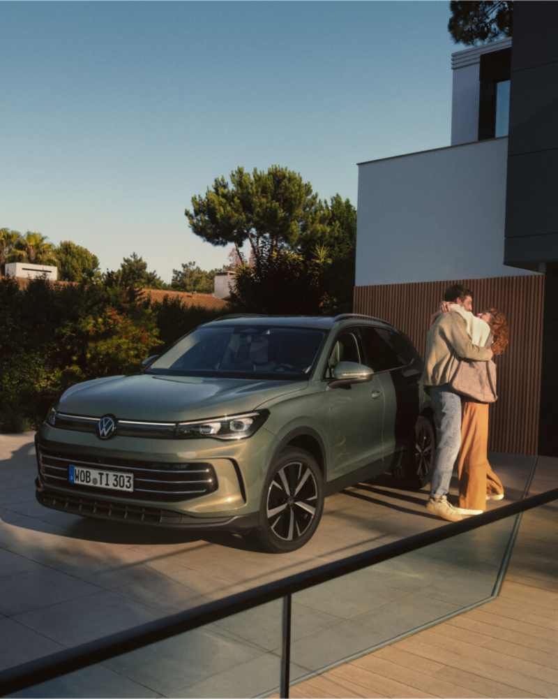 Una pareja junto a un Volkswagen Tiguan de color verde estacionado en el exterior