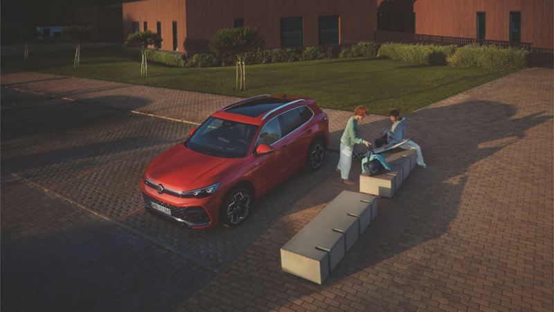 Una pareja en un parque junto a un Volkswagen Tiguan rojo