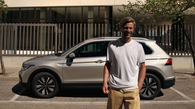 Chico sonriendo frente a un Volkswagen Tiguan gris aparcado en la calle