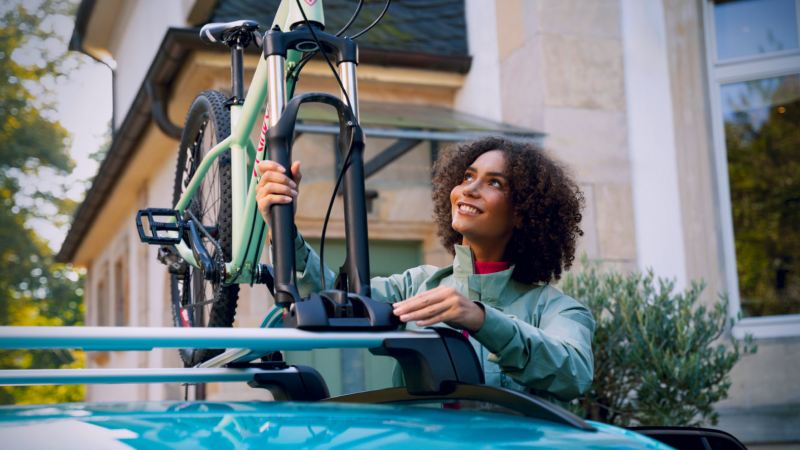 Una chica poniendo una bici en un portabicicletas en el techo de un Volkswagen