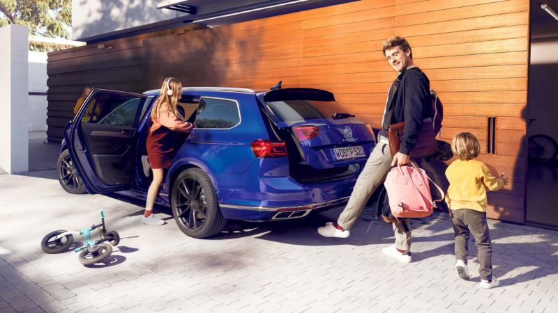 El niño se sube al Volkswagen Passat Estate, el hombre lleva bolsas y usa el pie para abrir el maletero con el Easy Open opcional.
