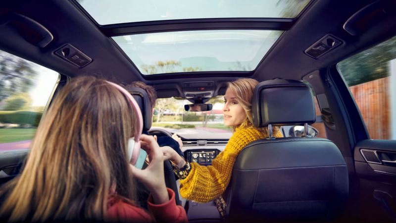 Familia sentada en el Volkswagen Passat Alltrack, vista del interior hacia adelante, el techo panorámico opcional ofrece luz y una vista del cielo.