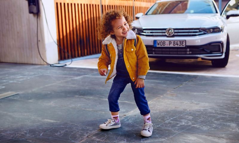 Niño sonriendo delante de un Volkswagen Passant Variant híbrido enchufable.