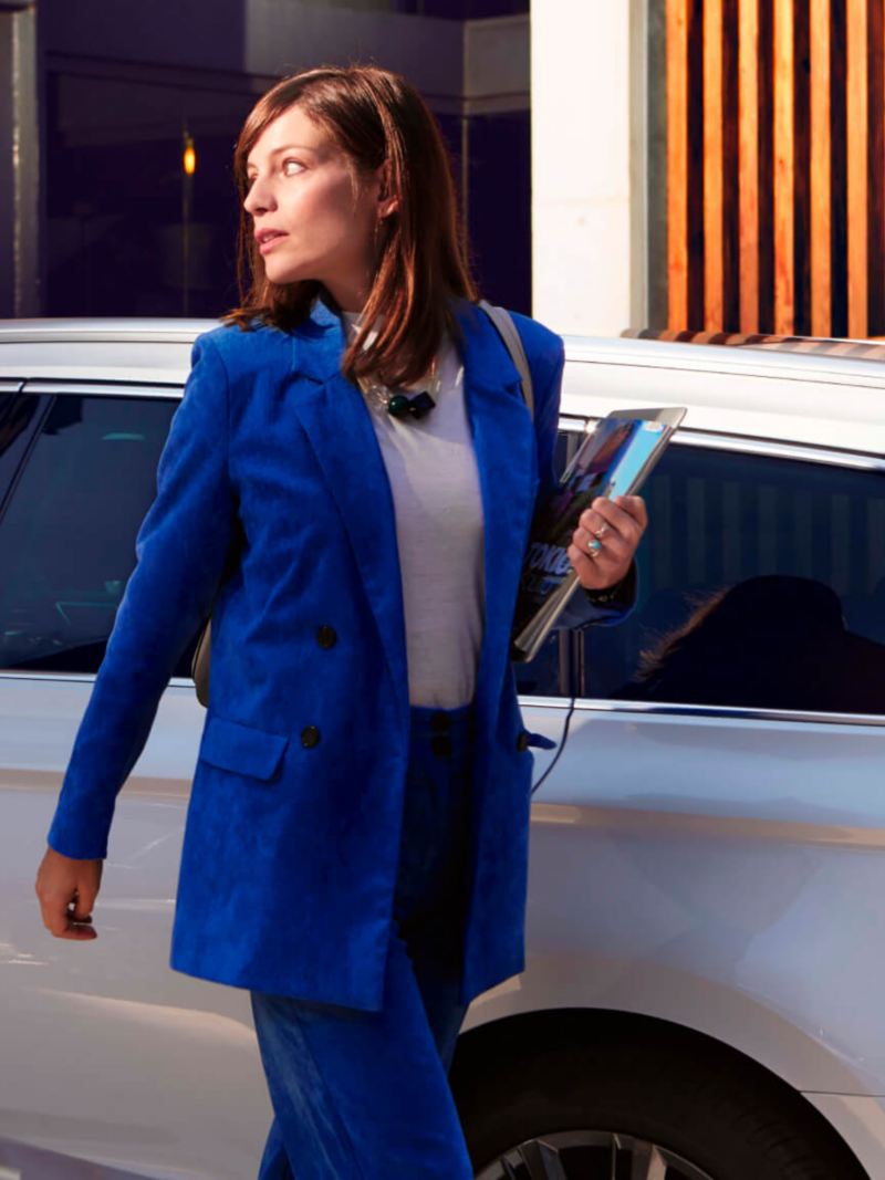 Mujer vestida de azul caminando delante de un Volkswagen Passat Variant de color blanco.