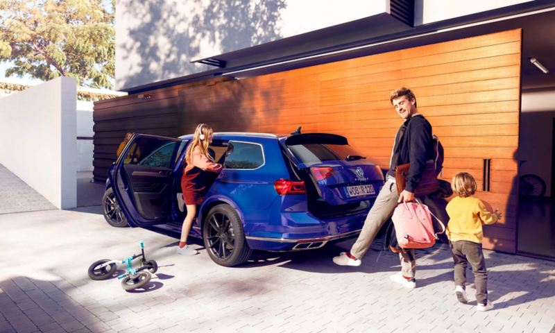 Familia interactuando con el Passat Variant Volkswagen. Padre y hijo jugando, guardando mochilas en el maletero, y mujer joven ingresando al auto escuchando musica.