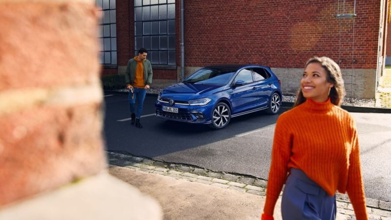 Una mujer y un hombre delante de un Volkswagen Polo de color azul oscuro estacionado en la calle