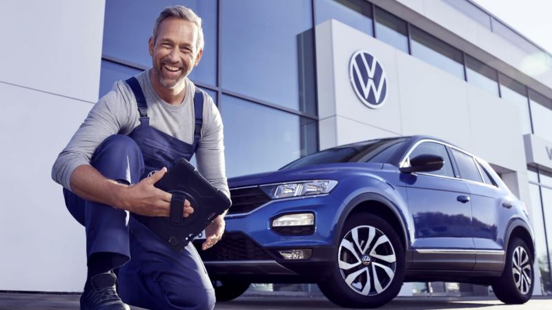 Un agente de servicio Volkswagen sonriendo delante de un T-Roc azul