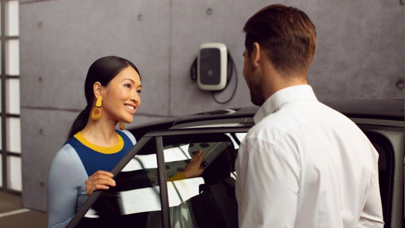 Mujer junto a la puerta abierta de un Volkswagen mientras habla con un mecánico