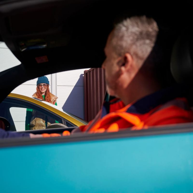 Un agente de servicio Volkswagen sentado en un coche mirando a una chica de pie