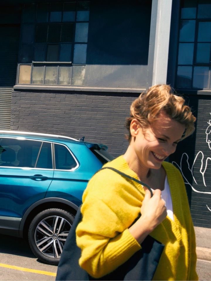 Chica sonriendo delante de un Volkswagen aparcado en la calle