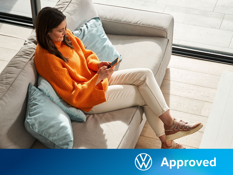 Una chica sentada en un sofa con un smartphone y el logo de Volkswagen Approved
