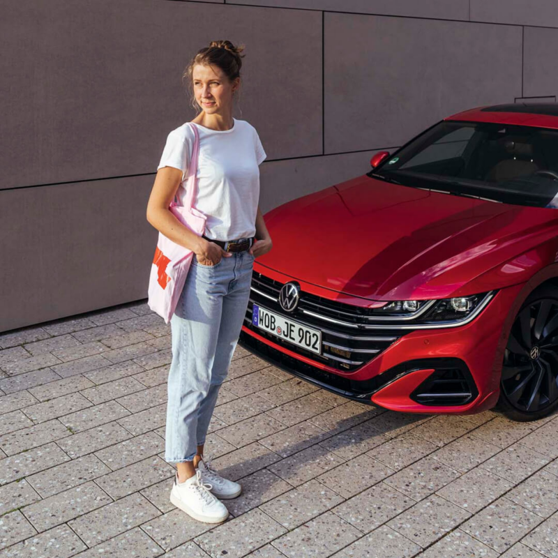 Chica de pie delante de un Volkswagen Arteon rojo