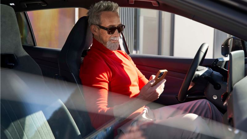 Un hombre se sienta en su Volkswagen estacionado con un teléfono móvil en la mano