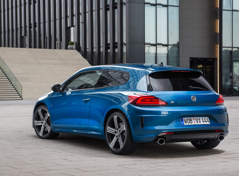 Un Volkswagen Scirocco azul visto por detrás aparcado delante de las escaleras de un edifico de oficinas