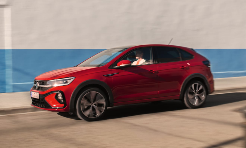 Un Volkswagen Taigo color rojo visto de costado parado delante de una pared blanca con linea azul