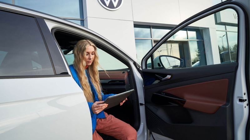 Una chica con una tablet sentada en un Volkswagen ID. con la puerta abierta