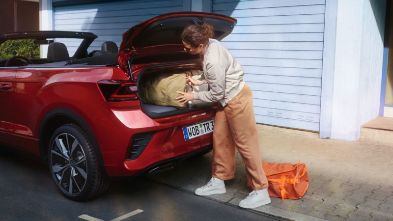 Chica cargando el maletero de un Volkswagen T-Roc Cabrio rojo