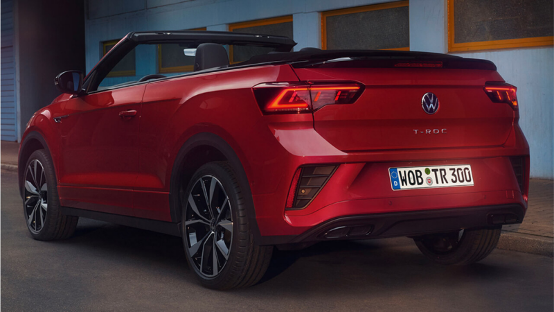 Un Volkswagen T-Roc Cabrio de color rojo visto desde la parte trasera estacionado en la calle con los faros traseros encendidos