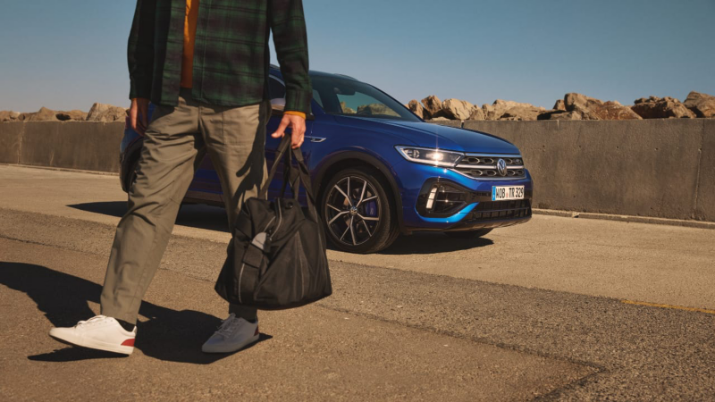 Un chico al lado de un T-Roc R azul estacionado en una carretera
