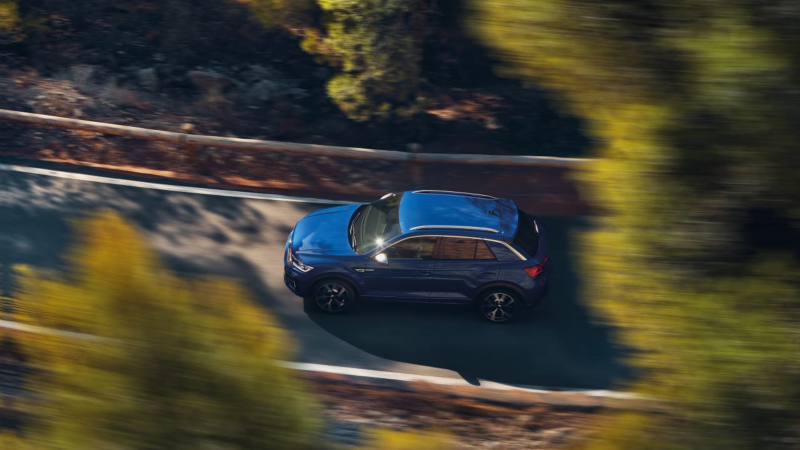 Un hombre subido a un velero y un Volkswagen T-Roc R azul al fondo aparcado en la playa