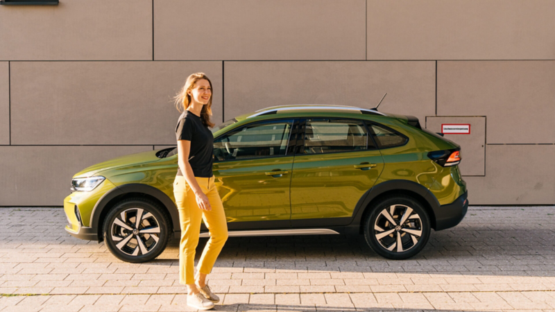 Una chica delante de un Volkswagen Taigo de color verde oliva estacionado en la calle