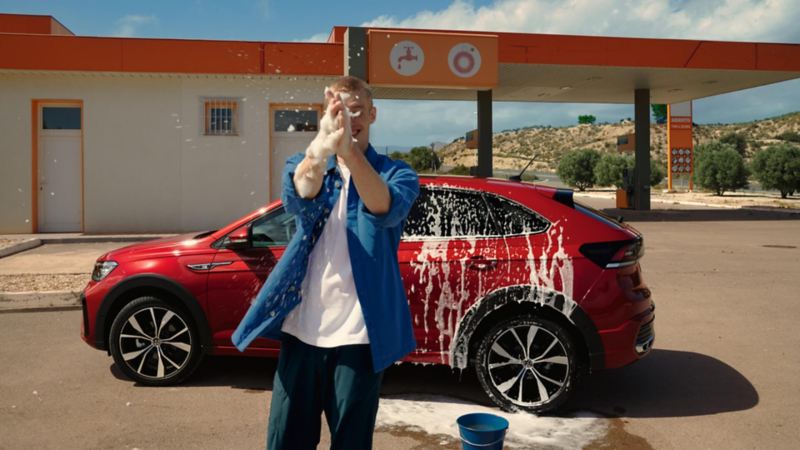 Una chico lavando un Volkswagen Taigo rojo en una gasolinera