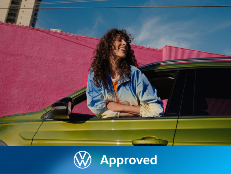 Una chica en la ventana de un Volkswagen de color verde con el logo de Approved
