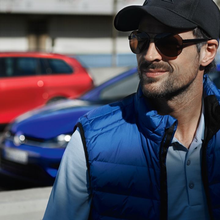 Chico con gorra y gafas de sol delante de unos modelos Volkswagen