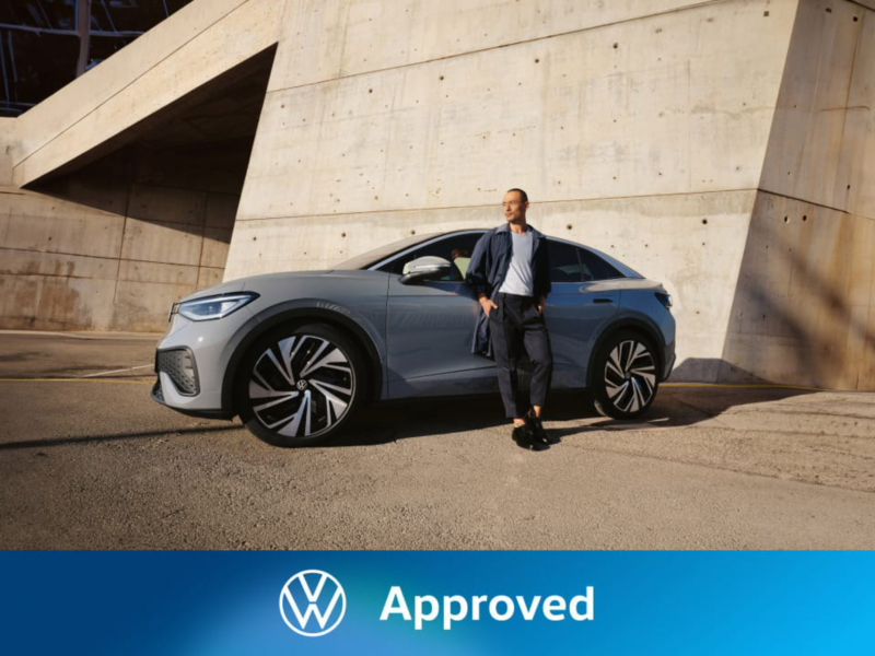 Un hombre junto a un Volkswagen de color gris estacionado en la calle