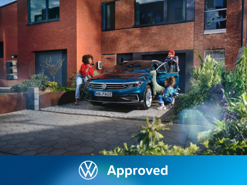 Una familia junto a un Volkswagen conectado a carga de color azul oscuro estacionado delante de una casa