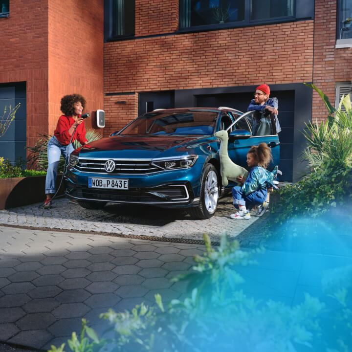 Una familia junto a un Volkswagen conectado a carga de color azul oscuro estacionado delante de una casa