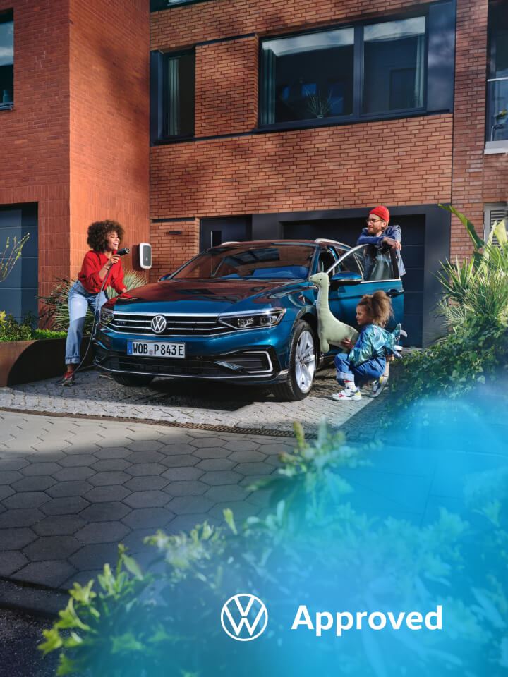 Una familia junto a un Volkswagen conectado a carga de color azul oscuro estacionado delante de una casa