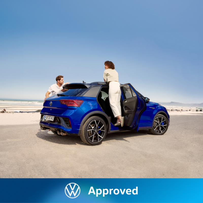 Una pareja en un Volkswagen gama R de color azul oscuro estacionado en la playa