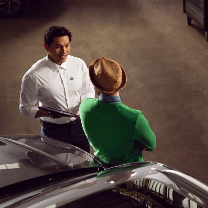Hombre apoyado en un Volkswagen mientras habla con un representante de Volkswagen vistos desde arriba