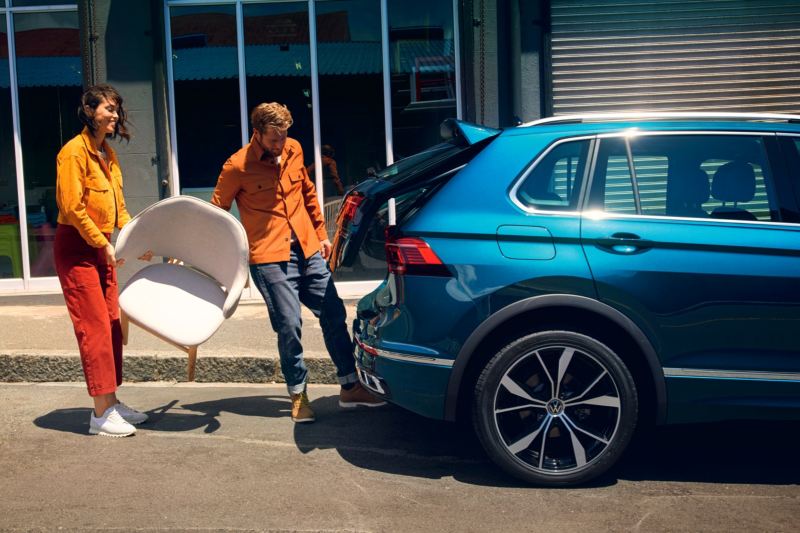 Una pareja con unas silla abriendo el portón trasero de un Volkswagen Tiguan eHybrid azul