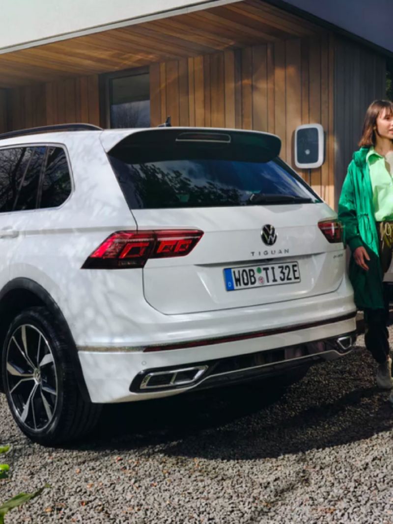 Dos chicas caminando detrás de un Volkswagen Tiguan híbrido enchufable aparcado y conectado a un Wallbox