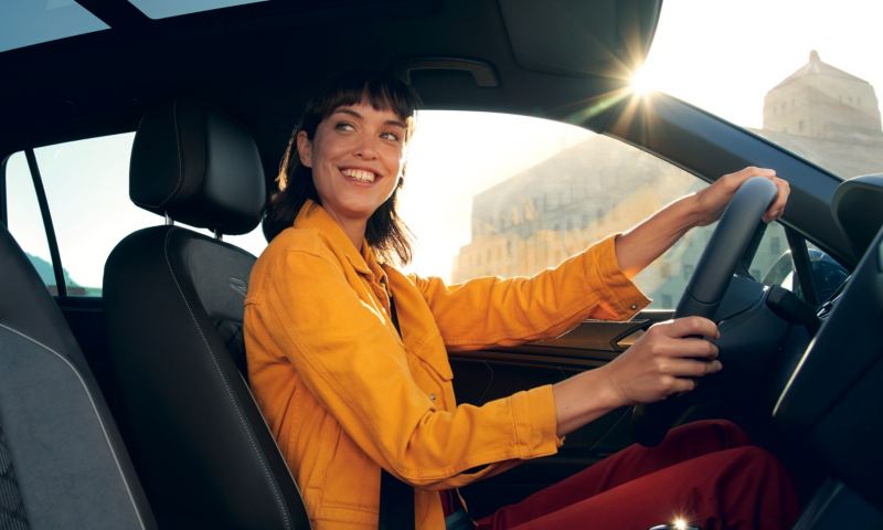 Chica con chaqueta amarilla sonriendo al volante de un Volkswagen Tiguan híbrido enchufable