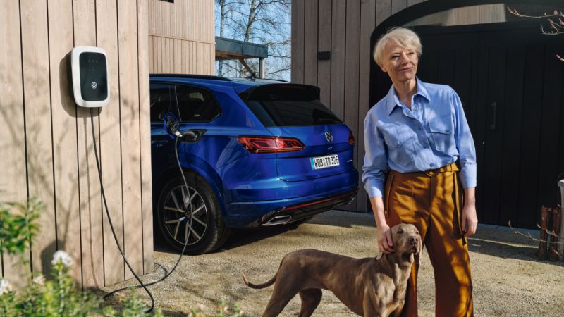 Mujer con perro delante de un Touareg azul conectado a un ID. Charger