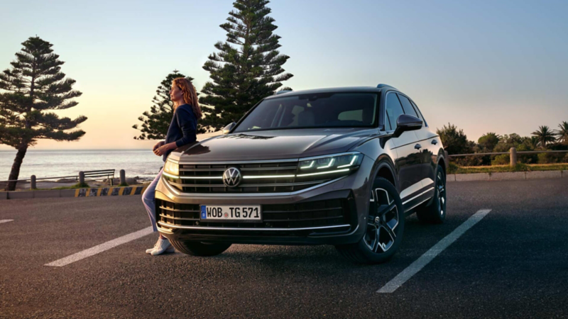 Un chica apoyada sobre un Volkswagen Touareg estacionado en una plaza de aparcamiento