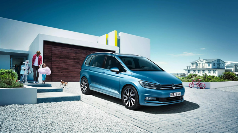 Una familia junto a un Volkswagen Touran de color azul estacionado fuera de una casa