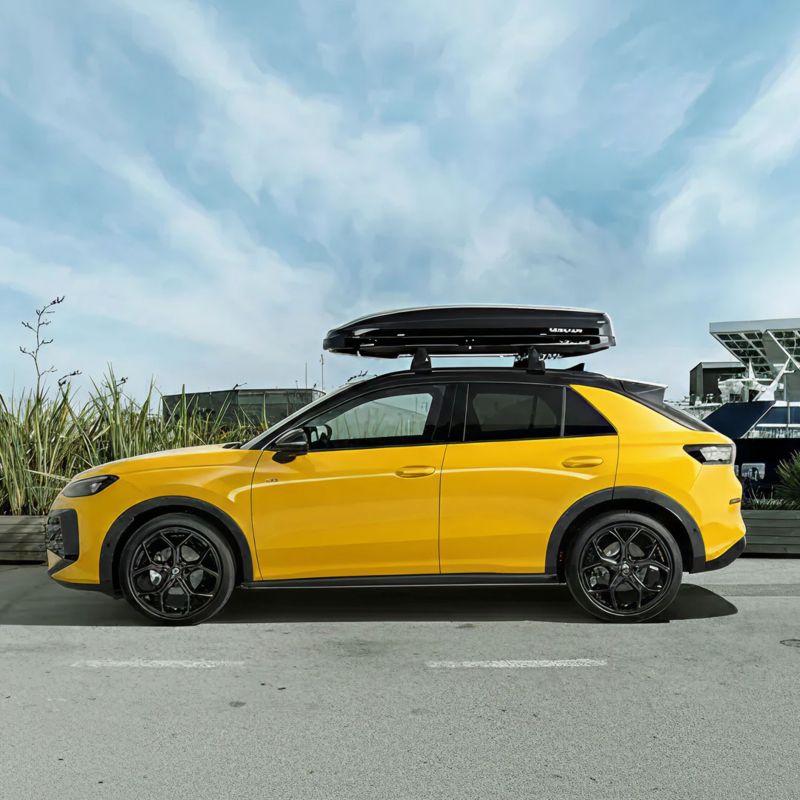 Un VW T-Roc amarillo con baúl de techo aparcado en una carretera – Accesorios T-Roc