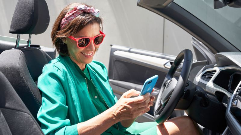 Chica vestida de verde y con gafas rojas mirando de el móvil dentro de un VW