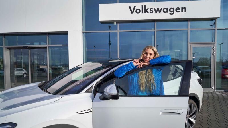 Mujer joven apoyado en la puerta de un Volkswagen delante de un servicio VW
