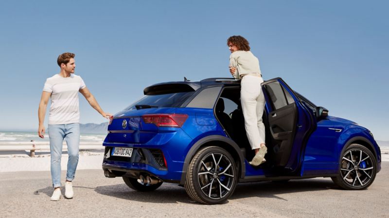 Pareja de jóvenes con su Volkswagen T-Roc R azul delante del mar